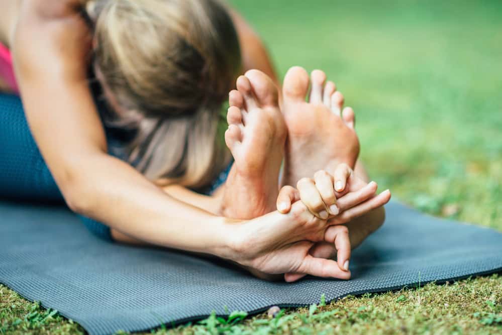 Woman doing Yoga, seated forward bend outside on a mat.