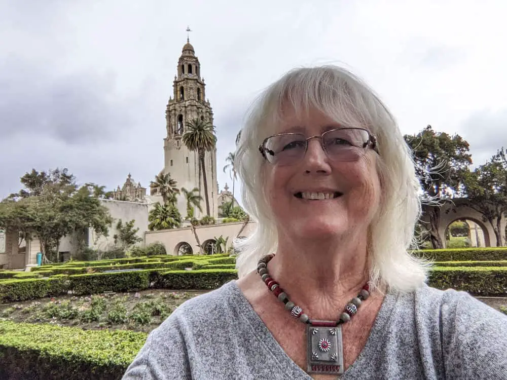 Nancy Ulrich, founder of SanDiegoing.com in Balboa Park's Alcazar Garden with the California Tower in the background.